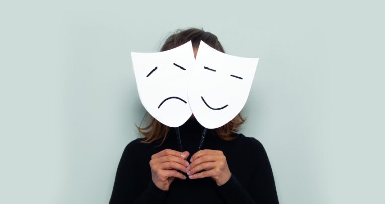 Photograph of figure concealed behind comedy and tragedy masks