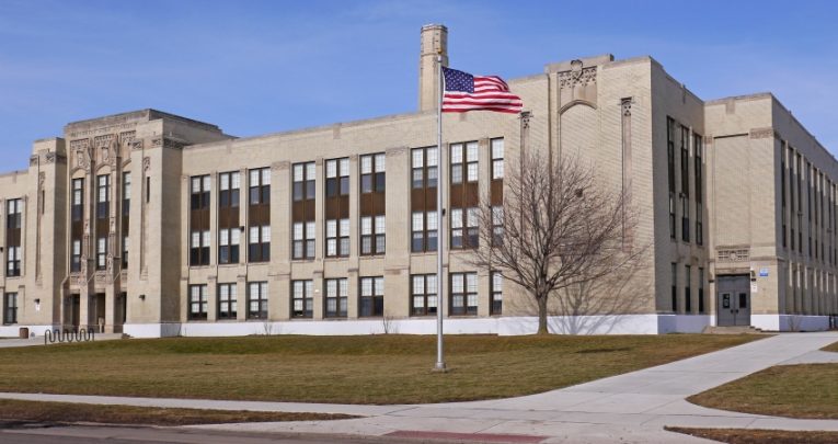longshot photograph of a US high school with an American flag flying in the grounds