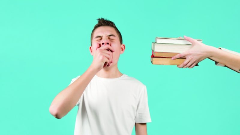 Photograph of a yawning boy being offered a selection of books