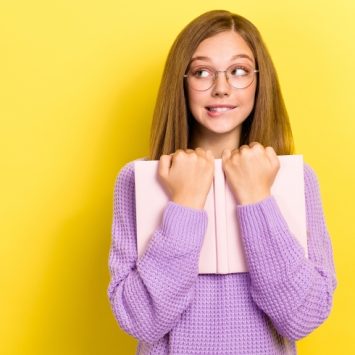 Photo of teenage girl with embarrassed expression holding a book