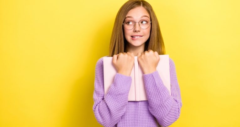 Photo of teenage girl with embarrassed expression holding a book