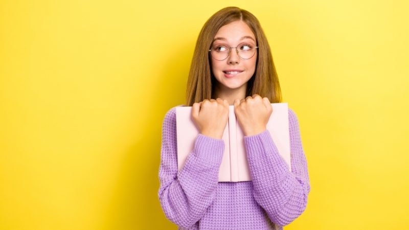 Photo of teenage girl with embarrassed expression holding a book