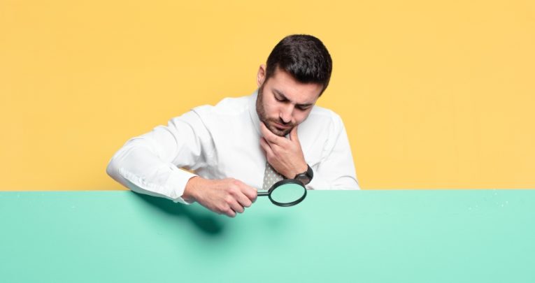 photo of besuited man inspecting a plain surface with a magnifying glass, representing Ofsted outstanding schools downgraded