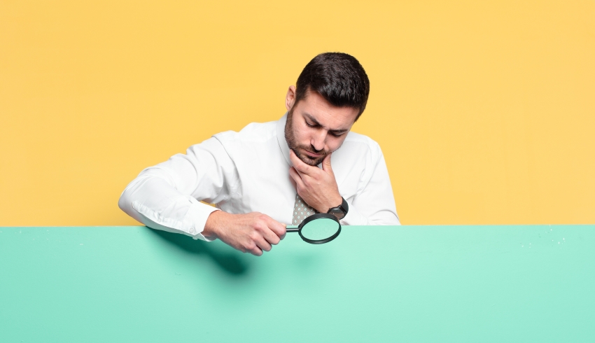 photo of besuited man inspecting a plain surface with a magnifying glass, representing Ofsted outstanding schools downgraded