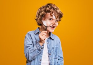 Blonde child looking through magnifying glass on bright orange background