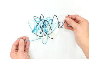 Two hands unravelling a small pile of light blue and dark blue string