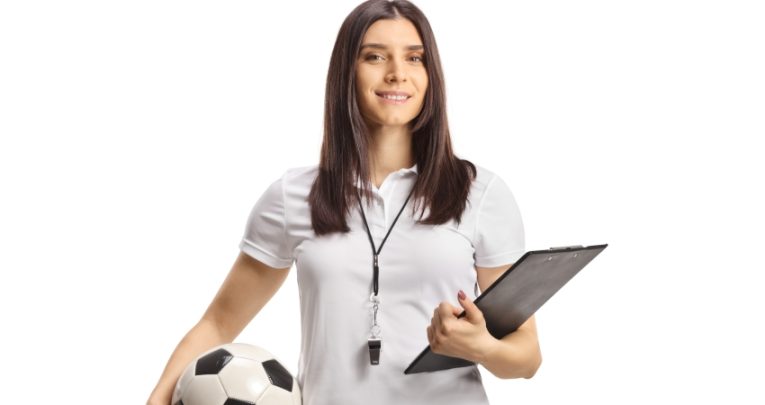 photo of woman in sportswear holding a football in one hand and a clipboard in the other