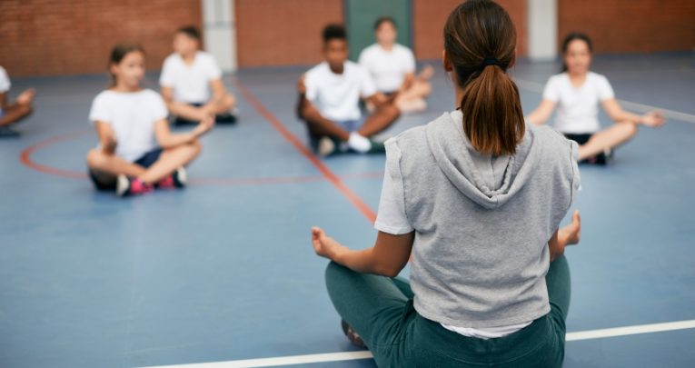 Photo of teacher modelling lotus position in front of a school class