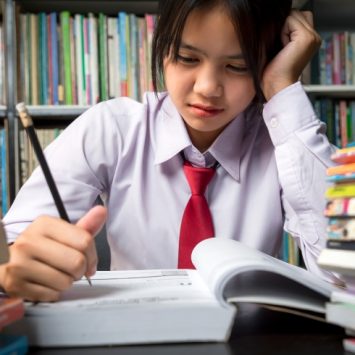 Close-up photo of teenage school student sat at desk, concentrating hard on reading a book