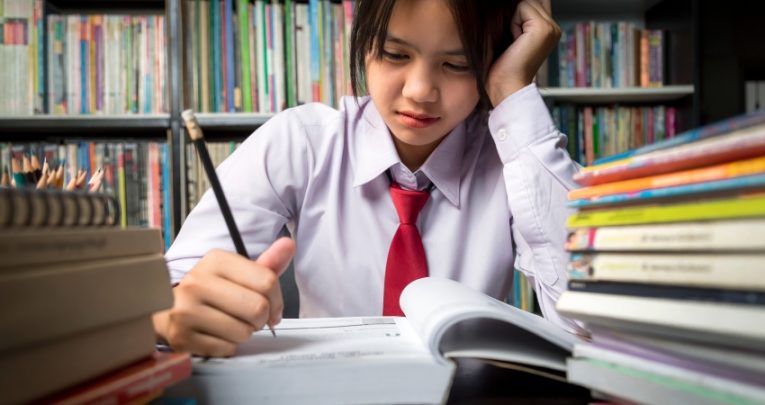 Close-up photo of teenage school student sat at desk, concentrating hard on reading a book