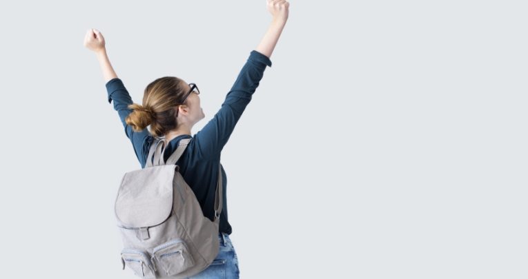 Photo taken from behind of teenage girl celebrating with arms outstretched