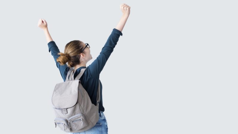 Photo taken from behind of teenage girl celebrating with arms outstretched