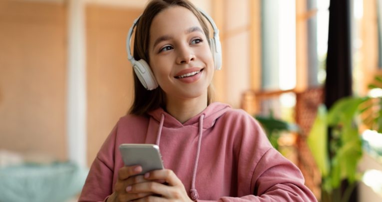 Photo of teenage girl using smartphone while wearing headphones