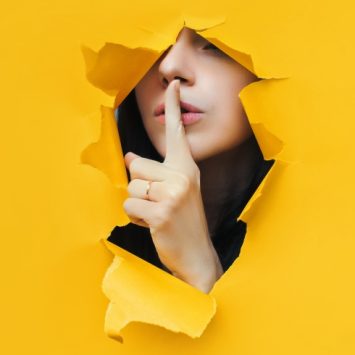 photo of someone shushing through an opening made in torn yellow paper