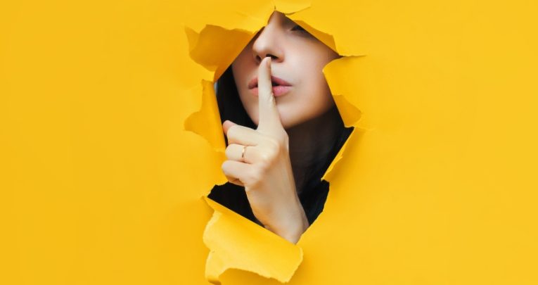 photo of someone shushing through an opening made in torn yellow paper