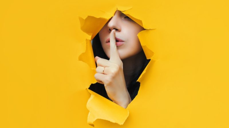 photo of someone shushing through an opening made in torn yellow paper