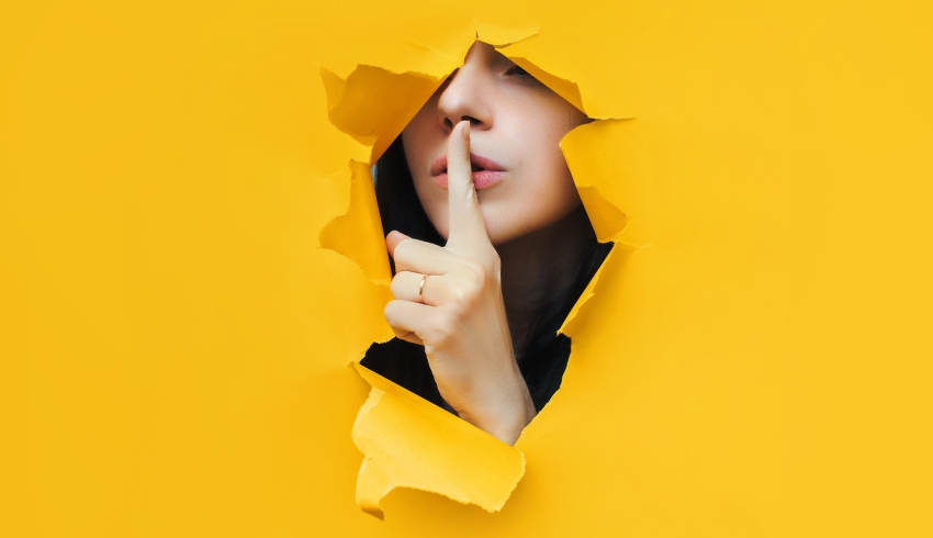 photo of someone shushing through an opening made in torn yellow paper