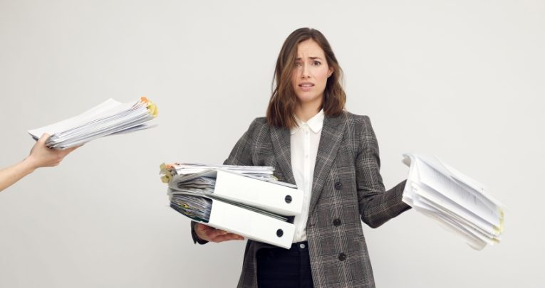 Photo of female teacher being handed too many folders and too much paperwork