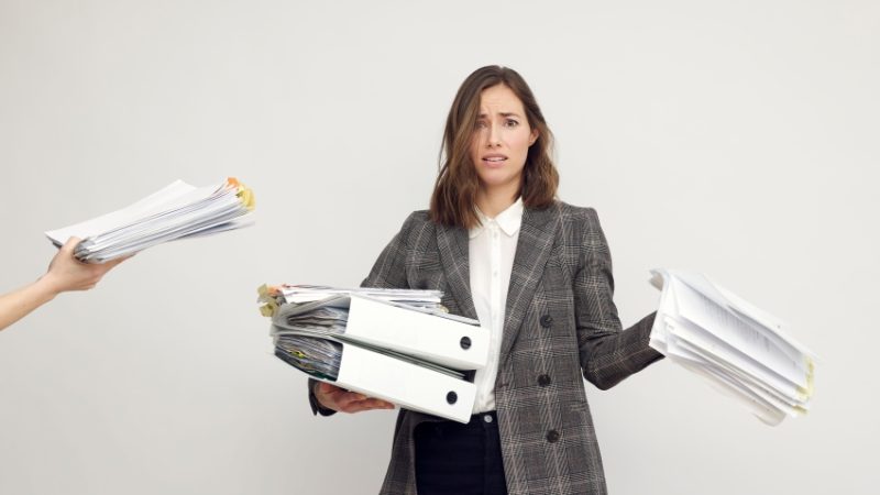 Photo of female teacher being handed too many folders and too much paperwork