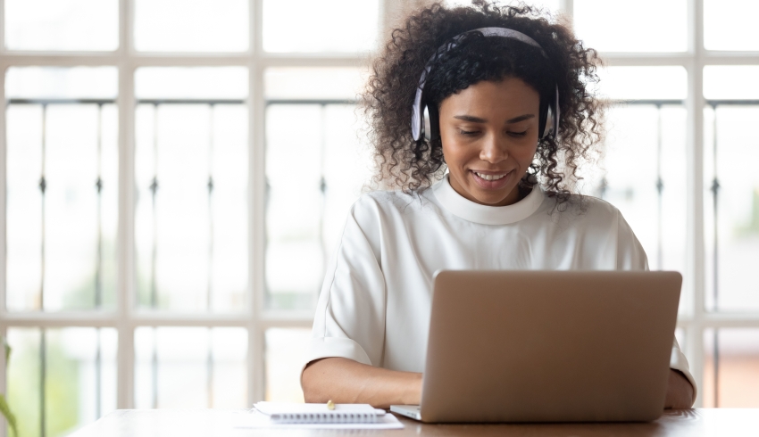 photo of young female teacher sat at a desk with a laptop while wearing a pair of headphones