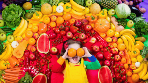 Kid surrounded by rainbow of fruit for Healthy Eating Week