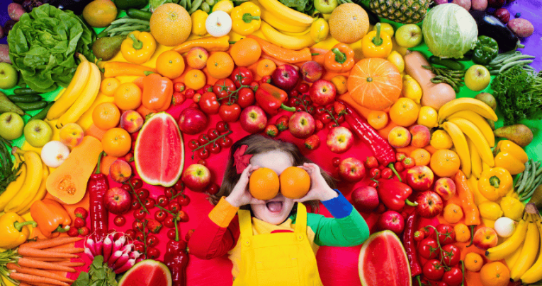 Kid surrounded by rainbow of fruit for Healthy Eating Week