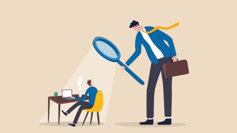 Illustration of large besuited figure holding a magnifying glass looming over a much smaller besuited figure working at a desk, representing Ofsted inspections