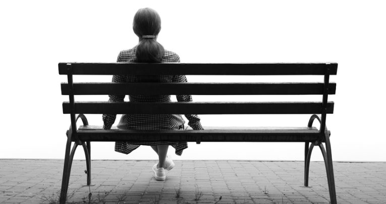 Photo of lonely figure sat on park bench, representing school absence