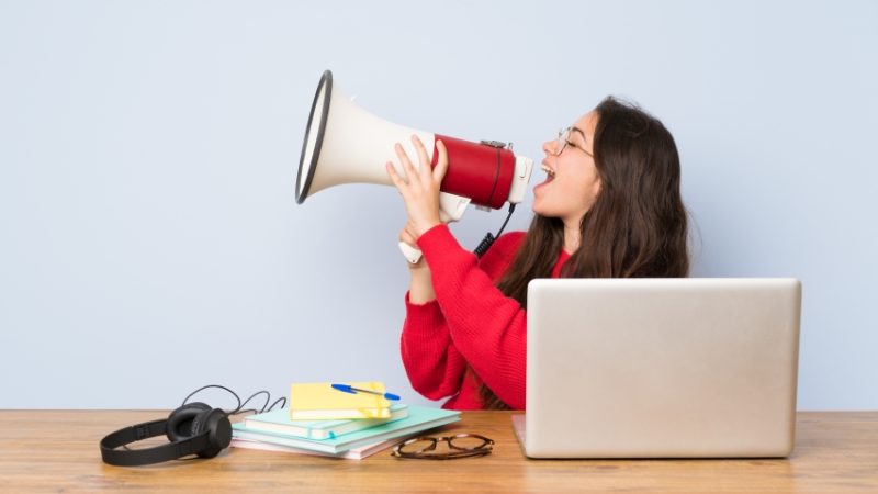 Photo of girl sat at desk talking into loudhailer