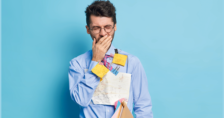 Photo of a fatigued-looking besuited male teacher yawning, with an assortment of Post-it notes stuck to his torso