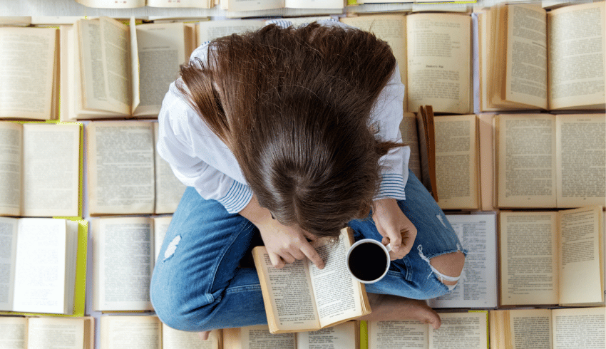 Teenager sitting on pile of books reading for Banned Books Week