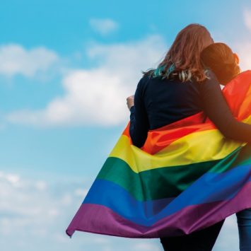 Shot of two teens facing away from camera wrapped in a rainbow Pride flag, representing inclusion in schools