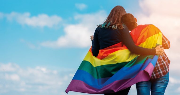 Shot of two teens facing away from camera wrapped in a rainbow Pride flag, representing inclusion in schools