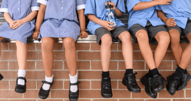 Children in school uniform sitting on wall, representing pupil premium