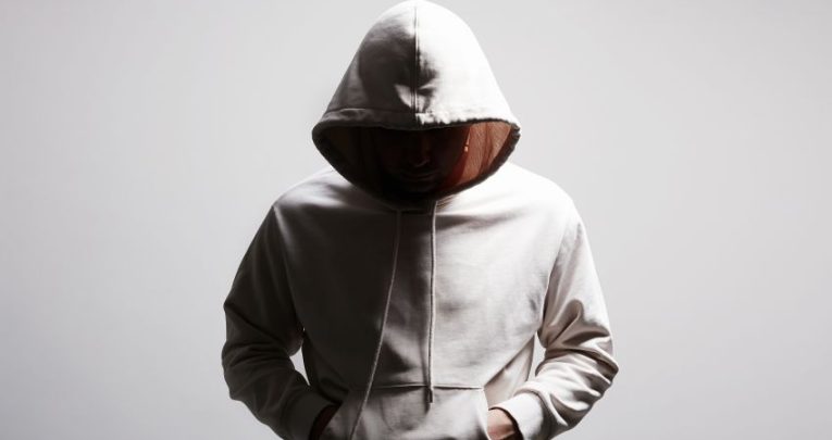 Photo of a partially-lit youth wearing a hoodie, representing violence in schools