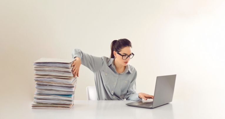 Woman shown sat in front of laptop going through a pile of written work, representing EHCP