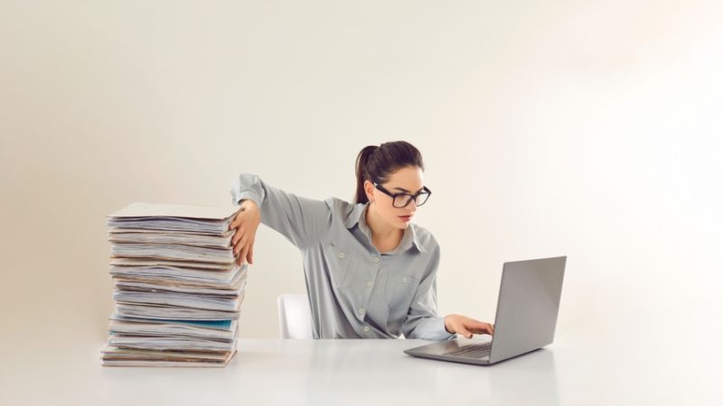 Woman shown sat in front of laptop going through a pile of written work, representing EHCP