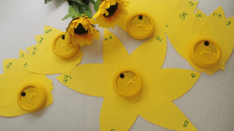 'Flower' for teaching phonics. Yellow paper petals with letters written on the tips; talking tins make the center of the 'flowers'