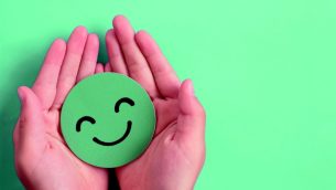Two hands cradling green smiley emoji, representing wellbeing in schools