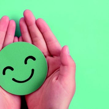 Two hands cradling green smiley emoji, representing wellbeing in schools