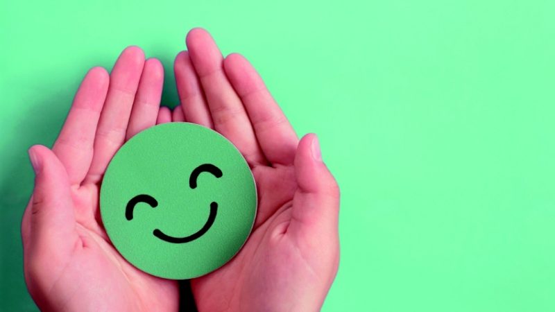 Two hands cradling green smiley emoji, representing wellbeing in schools