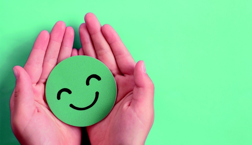 Two hands cradling green smiley emoji, representing wellbeing in schools