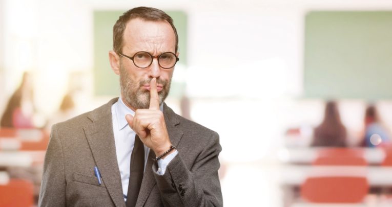 Photo of teacher with finger raised to his lips to illustrate notion of classroom silence