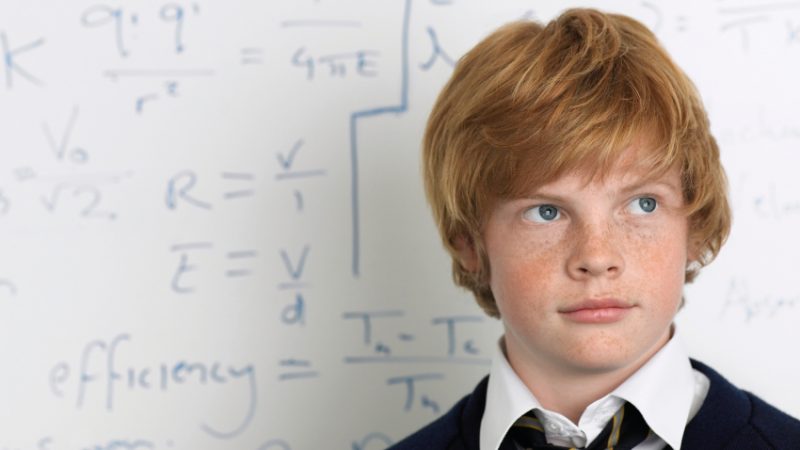Student standing in front of maths problem on board, representing maths problem solving