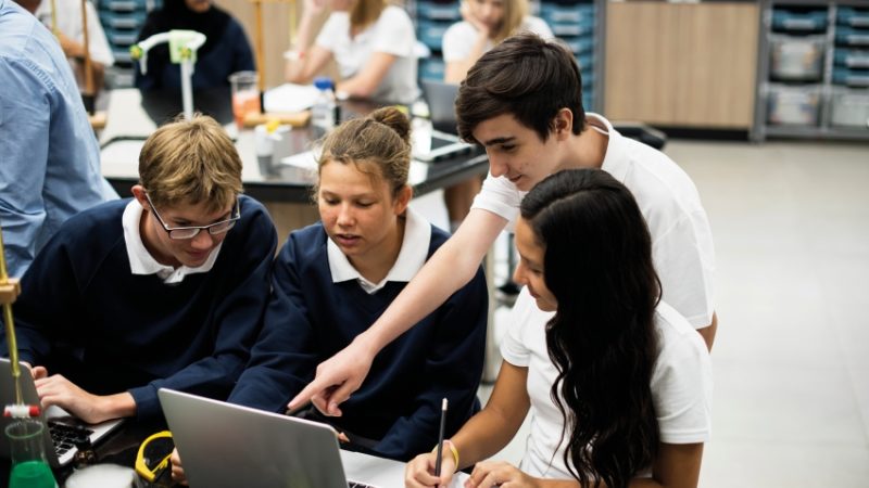 Photo of several teenage school students crowded round a laptop