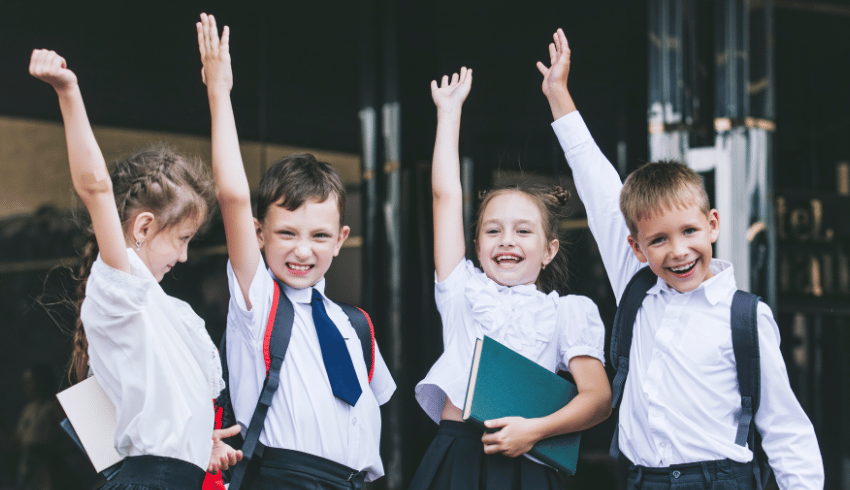Four happy children in school uniform raising their hands