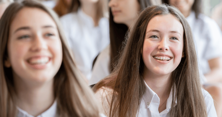 Two girls smiling in school assembly