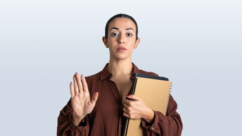 Professionally dressed woman holding papers with one arm while raising the other, as if to assert order