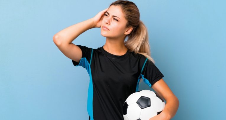 Photo of teenage girl dressed for football practice looking thoughtful, representing PE teaching
