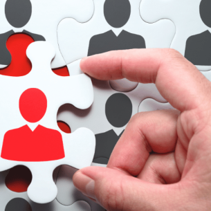 Hand selecting a puzzle piece with a red head and shoulders on it, representing teacher recruitment